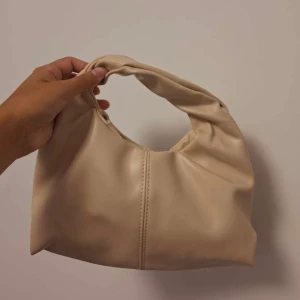 Trendig beige handväska stilren och mjuk modell - Superfin och stilren liten handväska i beige/aprikos ton. Perfekt till vardag eller fest – får plats med mobil, plånbok och lite smink. Väldigt mjuk och följsam i materialet, lite Bottega-stil. Inga skador eller fläckar oanvänd                                  Material: Mjuk faux läder (läderimitation)