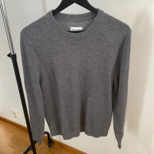 Grå merinoullströja These Glory Days - En stilren grå tröja från These Glory Days i mjuk merinoull. Klassisk rund halsringning och långärmad modell med ribbade muddar. Perfekt för lager-på-lager och passar till jeans eller chinos.