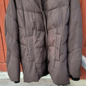 Brun pufferjacka från Northbrook - Säljer en brun pufferjacka från Northbrook Sports i storlek 48. Jackan har quiltad design, två fickor med knappstängning och dragkedja framtill. Perfekt för kyliga dagar och har en klassisk look som funkar till det mesta.