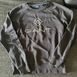 Brun sweatshirt från GANT - Säljer en brun sweatshirt från GANT med broderad logga framtill. Tröjan har rund halsringning, långa ärmar och ribbade muddar vid ärmslut och nederkant. Perfekt för en avslappnad och stilren look.