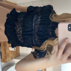 Svart spetsblus med volanger - Säljer en elegant svart spetsblus med volanger. Blusen har korta ärmar och ett vackert mönster i spets som ger en romantisk känsla. Perfekt för att piffa upp vilken outfit som helst!