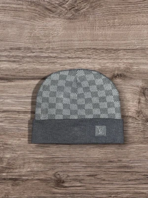Grå rutig mössa från L - Snygg grå mössa från L med klassiskt rutigt mönster och L framtill. Mössan är stickad och har en bred uppvikt kant. Perfekt för dig som gillar exklusiva accessoarer med stilren design.