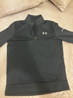 Svart half zip fleece Under Armour - Säljer en svart långärmad fleece från Under Armour med half zip och hög krage. Tröjan har en diskret bröstficka med dragkedja och logga på bröstet. Perfekt för kyliga dagar och sportiga outfits.