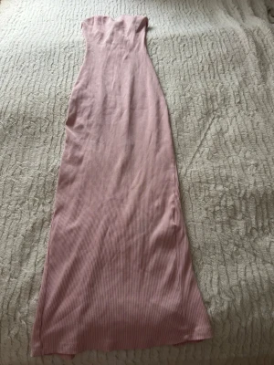 Rosa långklänning från FB Sister - Supersnygg rosa långklänning från FB Sister i ribbad bomull. Klänningen är axelbandslös  ränder samt en slits bak för extra rörelsefrihet. Perfekt för dig som vill ha en enkel men ändå chic look.