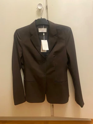 Mörkbrun kavaj från Boss - Snygg mörkbrun kavaj från Boss med klassisk krage och två knappar framtill. Jackan har två fickor och är helfodrad för en clean look. Perfekt för dig som vill ha en stilren och tidlös outfit. (Aldrig använd) Skriv för mer information eller prisförslag🙏