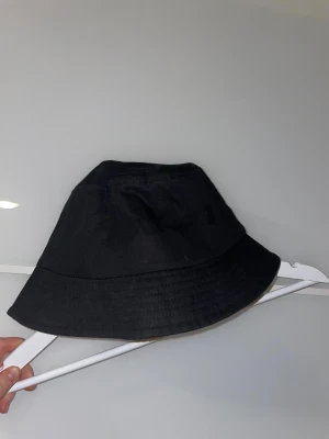 Svart Bucket hat från BikBok - En stilren svart bucket hat från BikBok i 100% bomull. Klassisk form med bredare brätte och diskreta sömmar runt om. Perfekt accessoar för att lyfta din outfit och skydda mot solen.