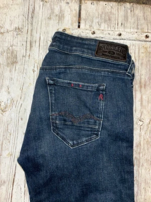 Replay blå jeans  - Säljer ett par klassiska blå jeans från Replay i modellen Rose. Jeansen har raka ben, fem fickor och snygga detaljer med Replay-logga på bakfickan och myntfickan. Materialet är slitstarkt jeans i bomull med en mörk tvätt och subtila kontrastsömmar.