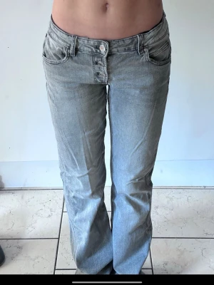 Grå jeans från Gina Tricot, bootcut - Säljer ett par gråa jeans från Gina Tricot i storlek 158. De har låg midja, bootcut-ben och flera knappar i gylfen. Jeansen är i klassisk denim med en snygg tvättad look och har fickor både fram och bak. Perfekta till en avslappnad stil.