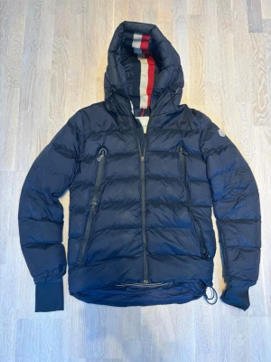Moncler Grenoble Camurac Jacket Size 2 (M) – Blue | Priced Accordingly - Selling an authentic Moncler Grenoble Camurac jacket in size 2, which corresponds to approximately size M. A premium technical jacket from Moncler’s Grenoble line, designed for performance, warmth, and a sporty luxury look. The jacket is used and has known defects, which are fully reflected in the price: Left pocket is damaged. Left side has been stitched/repaired. Please carefully check the pictures for full transparency. 