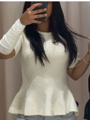 Vit ribbad topp med volangkant - Supersöt vit topp från H&M ribbad och volangkant nedtill. Modellen har rund halsringning och korta ärmar. Perfekt att styla med jeans eller kjol för en clean look. Materialet är mjukt och stretchigt, vilket gör den riktigt bekväm.