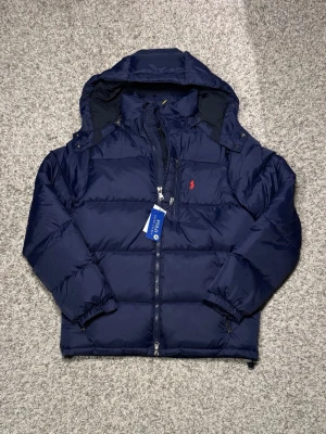Ralph Lauren Puffer Jacket - Mörkblå Puffer Jacket i storlek M, (passar även för S). Tags sitter kvar och den är i nyskick. Passar perfekt för vintern och våren. Nypris ligger på 6000kr. 