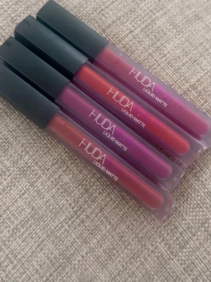 Huda Beauty Liquid Matte läppstift 4-pack använd bara två gångar - Fyra flytande matta läppstift från Huda Beauty i olika nyanser av rött, lila och rosa. Tuben är matt plast med svart lock och tydlig logga. Perfekt för dig som gillar intensiva färger och lång hållbarhet.