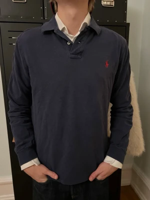 Ralph Lauren Polo Long Sleeve Shirt – Navy Blue – Custom Fit – Size M - Authentic Polo Ralph Lauren long sleeve polo shirt in classic navy blue with iconic red logo embroidery. • Custom Fit • Size: Men’s M • Color: Navy Blue • Long sleeves • 100% cotton • Buttoned polo collar • Timeless and versatile style Condition: Good used condition – normal signs of wear, no major flaws. Perfect for smart casual outfits, everyday wear, or preppy style lovers. A classic Ralph Lauren piece that never goes out of style. Details Brand: Polo Ralph Lauren Fit: Custom Fit Size: M 