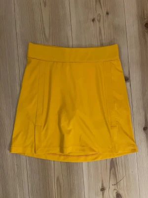 J.Lindeberg Amelie mid skirt - XS - Snygg gul kortkjol från J.Lindeberg i sportig stil. Kjolen har en enkel design med bred linning och diskret logga bak. Perfekt för dig som gillar färg och vill sticka ut. Tillverkad i ett mjukt och stretchigt material som känns bekvämt hela dagen.