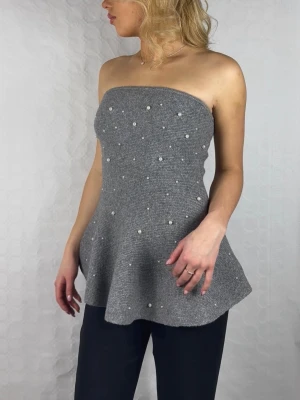 Grå stickad tubtopp med pärlor H&M - Supersnygg grå stickad tubtopp från H&M med utsvängd nederdel och pärldetaljer framtill. Toppen är axelbandslös och har en mjuk, ribbad känsla som ger en cool och trendig look. Perfekt att styla med jeans eller kostymbyxor.