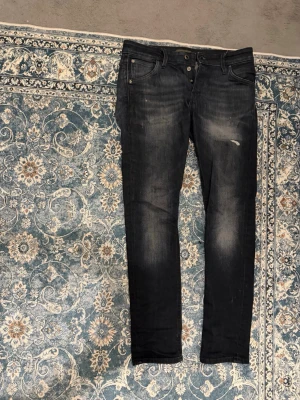 Slim Glenn svarta skinny jeans - Svarta skinny jeans från Slim Glenn med slitningar och snyggt tvättad look. Jeansen har klassisk femficksdesign, knappgylf och smal passform som sitter tajt längs benen. Perfekta för dig som gillar en modern och stilren vibe.