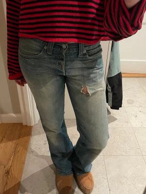 Levis ljusblå bootcut jeans - Säljer ett par klassiska Levis jeans i ljusblå tvätt med bootcut passform. Jeansen har låg midja, fem fickor och ett snyggt slitet hål på låret för en extra edge. Tillverkade i robust denim som ger en avslappnad vibe.