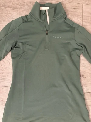 Grön Craft Core Gain Midlayer XS - Superskön grön Craft Core Gain Midlayer i storlek XS. Tröjan har halv dragkedja framtill, hög krage och är gjord i ett mjukt, stretchigt material. Perfekt för träning eller som lager under jackan. Helt oanvänd med prislapp kvar. Nypris 260 kr.