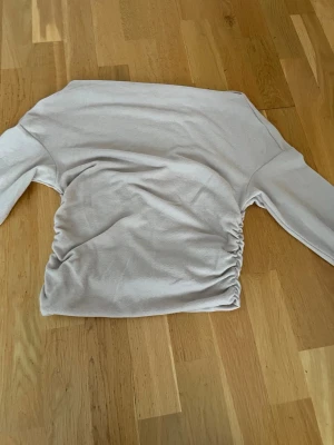 Beige långärmad topp med rynk - Säljer en beige långärmad topp med rynkade detaljer på sidan. Toppen har en rak halsringning och är figurnära i modellen. Materialet känns mjukt och stretchigt, perfekt för en clean och enkel look.