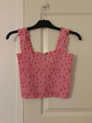 Blommig topp - Jättesöt rosa blommig topp som tyvärr inte används längre. Den har ett mycket bra skick, ser ny ut! Toppen är lite croppad och har ett stretchigt material vilket gör att den även kan bäras om man har storleken M.