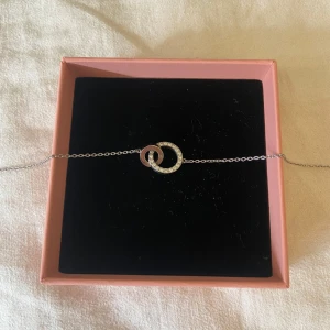Silverhalsband från Edblad  - Snyggt och stilrent halsband i silverfärg med två sammanlänkade cirklar, varav en är dekorerad med glittrande stenar. Tunn kedja och minimalistisk design som passar perfekt till din vardagsstil. Levereras i en rosa ask.