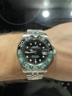 Seiko GMT-Master II klocka stål - Snygg Seiko GMT-Master II inspirerad klocka i rostfritt stål med svart urtavla och tvåfärgad svart och grön vridring. Klockan har datumfönster med förstoringsglas, tydliga index och länkarmband i metall. Perfekt för dig som gillar sportig och klassisk stil. Helt Ny och kommer i en fin låda.