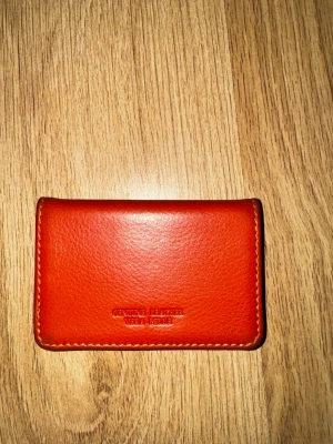 Orange skinnplånbok Vera Pelle - Snygg orange plånbok från Vera Pelle i äkta skinn. Plånboken har en stilren och enkel design med kontrastsömmar runt kanterna. Perfekt storlek för kort och sedlar, och den känns både trendig och klassisk.