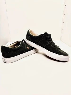 Mörkgröna mocka sneakers från Polo Ralph Lauren - Snygga mörkgröna sneakers från Polo Ralph Lauren i mocka med vit sula och klassisk logga broderad på sidan. Skorna har rund tå, snörning och en stilren design som passar till det mesta.