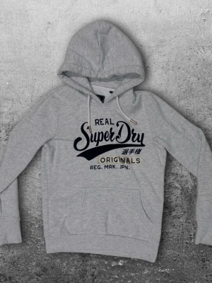 Superdry hoodie XS - En snygg Superdry hoodie i storlek XS. Färg grå/vit med små guldiga detaljer. Mycket bra skick! 😀