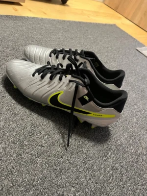 Nike Tiempo fotbollsskor silver/gul - Nike Tiempo fotbollsskor i silver med svarta och neongula detaljer. Skorna har snörning och är designade för att ge bra grepp på planen. 