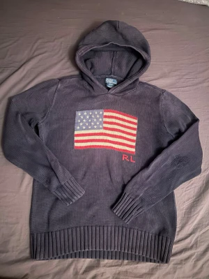 Stickad hoodie från Polo Ralph Lauren -  Stickad Polo Ralph Lauren äldre model med amerikanska flagan på. Ärmen är sliten som man ser på sista bilden. L i BARNSTORLEK 14-16. Skicka gärna frågor om ni undrar något 