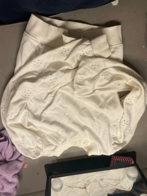 Vit sweatshirt med broderade hål - Säljer en vit sweatshirt från Gina Tricot med broderade håldetaljer i blommönster. Tröjan har ribbade muddar vid hals, ärmslut och nederkant. Perfekt för dig som gillar en enkel men ändå unik stil.