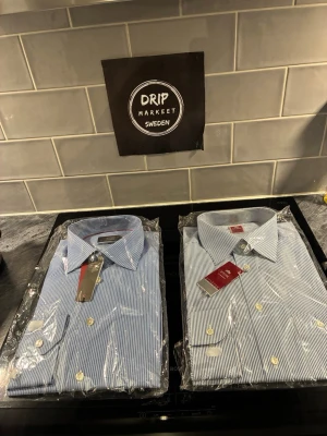 Blå-vitrandiga skjortor från Eton - Klassiska blå-vitrandiga skjortor från Eton köpt för 3500 kr styck.kommer i paketpris med vit knappstängning och krage. Skjortorna har lång ärm och är tillverkad i bomull för en skön och stilren känsla. Perfekt för dig som gillar tidlös design och snygga detaljer.