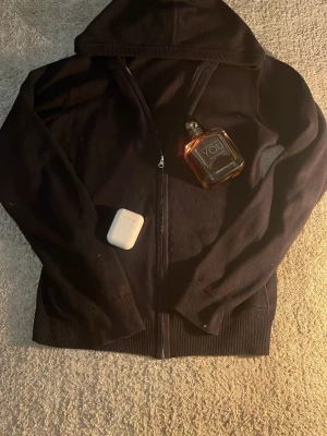 Svart hoodie från RYVLS Stockholm - Svart hoodie med dragkedja från RYVLS Stockholm. Klassisk modell med huva och ribbade muddar vid ärmslut och nederkant. Perfekt för en chill och avslappnad stil.