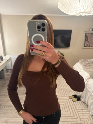 Brun ribbad långärmad topp - Snygg brun ribbad topp med lång ärm och fyrkantig ringning. Figurnära passform som framhäver siluetten. Perfekt att styla med jeans eller kjol för en trendig look.