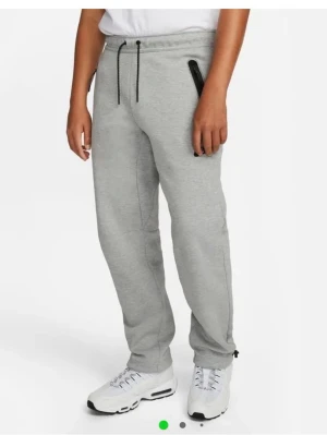 Grå mjukisbyxor från Nike - Snygga grå mjukisbyxor från Nike med svarta detaljer, dragsko i midjan och dragkedjeförsedda fickor. Byxorna har en relaxed passform och är tillverkade i mjukt bomullsmaterial. Perfekta för chill eller träning.