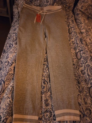 Grå mjukisbyxor från Iconic Sport - Mjukisbyxor i ljusgrått från Iconic Sport med vita detaljer i midjan och vid bensluten. Byxorna har snörning i midjan och är tillverkade i mjukt bomullsmaterial. Perfekta för chill eller träning, med relaxed passform och klassisk look.