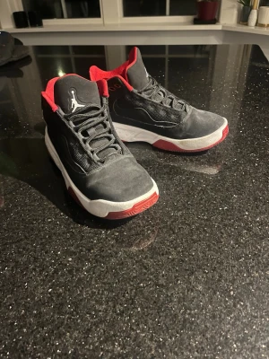 Svarta och röda Jordan sneakers - Snygga svarta sneakers från Jordan med röda detaljer och vit sula. Skorna har snörning, rund tå och klassisk Jumpman-logga på sidan och plösen. Ovandelen är i syntet och textil för en sportig look.