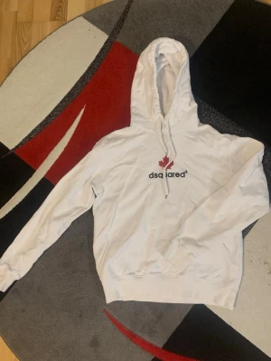 Dsquared2 hoodien - Snygg vit hoodie från Dsquared2 med huva och dragsko. På bröstet finns ett tryck med röd lönnlöv och Dsquared2-loggan. Hoodien har ribbade muddar vid ärmslut och nederkant. Perfekt för en chill och trendig look. Självfallet äkta. 9/10 skick inget tecken på användning. 