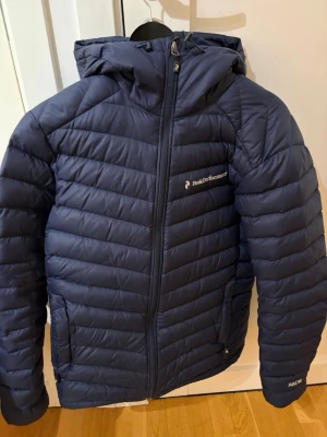 Mörkblå dunjacka från Peak Performance - Mörkblå dunjacka från peak performeance Åre, i storlek small. Använd men inga tecken på slitage.