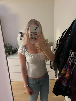 Topp Brandy Melville - Söt vit topp med omlottkänsla och korta puffärmar. Toppen har en bred, rundad urringning och sitter figurnära över kroppen. Perfekt att styla med jeans eller kjol för en trendig look. One size så alla brandys kläder är deeet