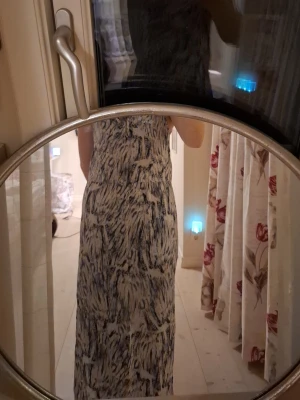 Långklänning med mönster från KappAhl - Säljer en långklänning från KappAhl i vitt med mörkblått abstrakt mönster. Klänningen har en rak passform och är ärmlös, perfekt för varma dagar. Materialet känns mjukt och bekvämt mot huden.