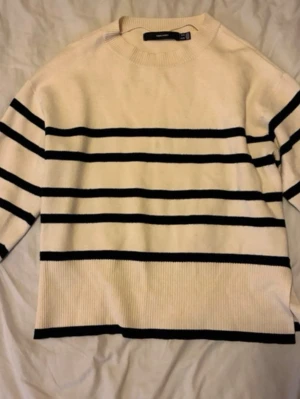 Randig stickad tröja från Vero Moda - Säljer en krämvit stickad tröja från Vero Moda med svarta horisontella ränder. Tröjan har en avslappnad passform, rund halsringning och ribbade muddar. Perfekt för dig som gillar en enkel men snygg look.