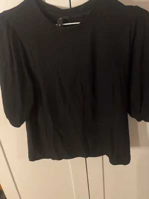 Svart croppad topp med puffärm - Säljer en svart croppad topp med puffiga korta ärmar och rund halsringning. Enkel och stilren design som passar till många olika outfits. Skön och mjuk känsla, perfekt för dig som gillar trendiga toppar.