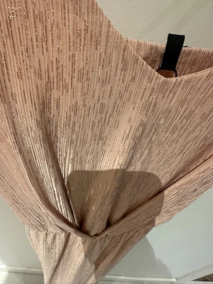 Glittrig champagneklänning Vero Moda-Ny! - Supersnygg glittrig klänning från Vero Moda i en champagnefärgad ton. Klänningen har omlott-ringning och smickrande midjeresår. Materialet är glittrigt och ger ett lyxigt intryck, perfekt för speciella tillfällen. Lätt plisserad struktur och mjukt fall.