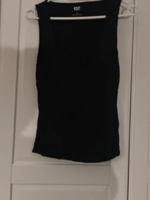 Svart linnetopp från 157 - En enkel och stilren svart linnetopp från 157. Toppen är ärmlös med rund halsringning och har en tight passform. Tillverkad i mjuk viskosblandning med lite stretch för extra komfort. Perfekt att matcha med jeans eller kjol.