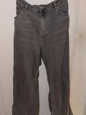 Gråa wide jeans från Monki, storlek 33 - Säljer ett par gråa jeans från Monki i storlek 33. De har en loose och wide passform med raka ben och klassiska 4 fickor. Tillverkade i 100% bomull för en skön och avslappnad känsla. Perfekta för dig som gillar en chill och trendig stil.