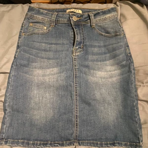 Blå jeanskjol från Voggo Denim - Säljer en klassisk blå jeanskjol från Voggo Denim med fem fickor, bälteshällor och snygga kontrastsömmar. Kjolen har en slits bak för extra rörelsefrihet och stängs med knapp och dragkedja. Materialet är bomull, polyester och elastan för skön stretch. 💙