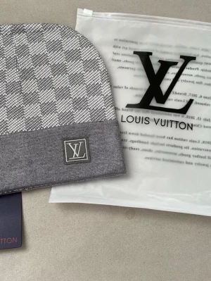 Grå rutig mössa - Snygg grå mössa med klassiskt rutigt mönster och logga framtill. Mössan har en bred ribbad kant och är perfekt för dig som vill ha en stilren accessoar med lyxig känsla.