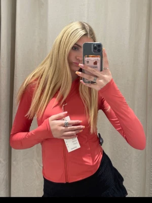 Oysho - Röd korallfärgad vindjacka med dragkedja - Snygg röd/rosa, egentligen en korallfärgad vindjacka med hel dragkedja framtill och högt krage från märket Oysho helt oanvänd. Jackan har två sidofickor med dragkedja och är tillverkad i ett lätt syntetmaterial. Perfekt för blåsiga dagar och har en clean, sportig look med långärmade ärmar.